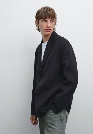 Zwarte wollen blazer met een enkele knoop, notch-lapels en zijzakken, gecombineerd met een witte T-shirt en lichtblauwe denim jeans.