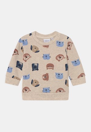 Sweat-shirt beige présentant un motif répété de divers visages d'animaux en bleu et marron. Tissu doux avec poignets et ourlet côtelés.