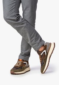 Sportliche Schuhe aus einer Kombination von braunem Wildleder und Mesh, mit einer klobigen weißen Zwischensohle und brauner Gummisohle; orangefarbener Akzent an der Zunge.
