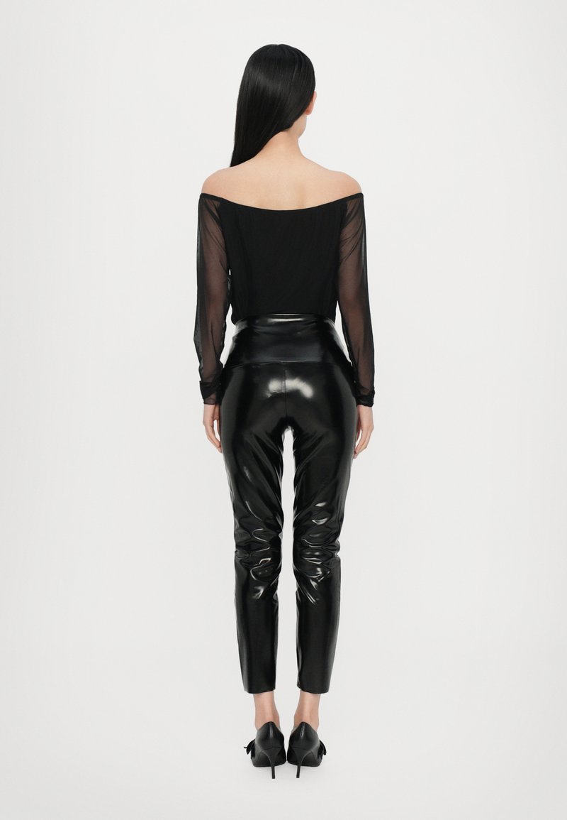 Top nero trasparente con spalle scoperte e maniche lunghe abbinato a pantaloni neri a vita alta lucidi, caratterizzati da una vestibilità slim e una superficie morbida.