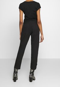 Pantalones cargo negros de corte relajado, con bolsillos laterales y puños con botones, combinados con una camiseta negra de manga corta.