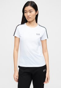 Balta īsroku T-krekls ar melnām un sarkanām strīpām plecu rajonā, kreisajā krūšu daļā neliels EA7 logo.