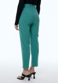 Hoge taille teal broek met een rechte pasvorm, met een gladde textuur en een achterzak, gecombineerd met zwarte haksandalen.