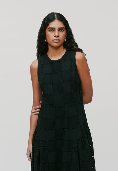 Schwarzes ärmelloses Kleid mit einem strukturierten Rautenmuster, das Ausschnitte, einen runden Ausschnitt und einen ausgestellten Saum aufweist. Glatte Stoffoberfläche.