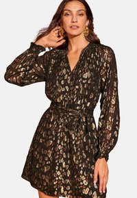 Černé šaty s pozlaceným leopardím potiskem, dlouhými nabíranými rukávy, výstřihem do V a opaskem v pase. Průhledná, texturovaná tkanina zvýrazňuje design.