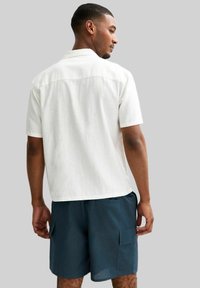 Witte short-sleeve shirt met een relaxte pasvorm, voorzien van een detail op de rug en gecombineerd met marineblauwe cargoshorts. Textuurstof.