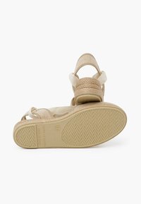 Espadrilky v béžové barvě se tkaným textilním svrškem, nastavitelnými popruhy a strukturovanou gumovou podrážkou. Jednoduchý a funkční design.