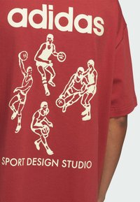 Červené bavlněné tričko s bílou grafikou basketbalistů v různých pozicích a textem "adidas SPORT DESIGN STUDIO" níže.