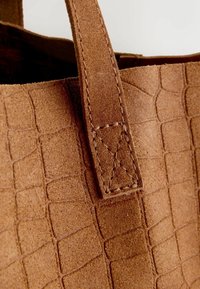 Braune Wildleder-Tasche mit strukturiertem, geprägtem Muster. Sie verfügt über einen genähten Griff und eine geräumige Öffnung.