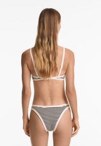 Bikini set s prugastim uzorkom u crno-krem boji, s podesivim trakama i minimalističkim dizajnom koji naglašava jednostavnost i udobnost.