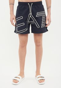Marina badshorts med stor vit text "EAT", elastiskt midjeband och snörning. Slät tyg med avslappnad passform och sidofickor.