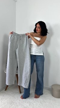 Grijze sweatpants met een elastische tailleband en trekkoord, met een losse pasvorm en zachte textuur, worden voor een model gehouden.
