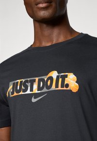 Sort bomulds T-shirt med et stort "JUST DO IT." grafik i orange og grå med et Nike-logo. Enkel crew neckline, glat tekstur.
