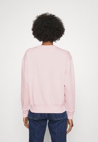 Rosa sweatshirt med rundad halsringning, sänkta axlar och ribbade ärmslut. Mjuk textur, avslappnad passform, med ett enfärgat mönster.