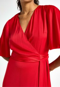 Rød indpakningskjole lavet af glat stof, med korte flæsermer, en dyb V-halsudskæring og en knyttet taljeaccent.