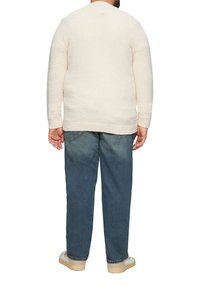 Cremfarbener, strukturiert gestrickter Pullover mit langen Ärmeln, Rückansicht. Kombiniert mit blauen Jeans und hellen Schuhen. Einfaches, lässiges Design.
