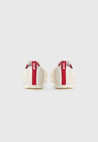 Baskets beiges avec des accents rouges, en suède et en maille, avec un col rembourré et une semelle en caoutchouc texturée. Logo "DIESEL" sur l'onglet du talon.