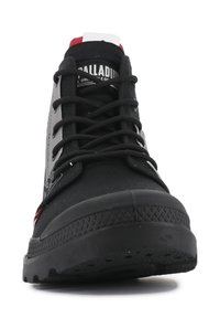 Czarne sneakersy w stylu high-top z teksturowaną gumową podeszwą, dopasowanymi czarnymi sznurówkami oraz czerwonymi i białymi akcentami na pięcie i języku.