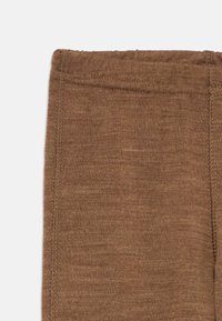 Közelkép barna kötött anyagú leggings derékpántjáról és varrási részleteiről, fehér háttér előtt.