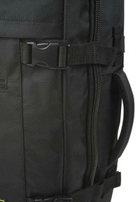 Mochila negra con un material texturizado, múltiples correas, un bolsillo con cremallera lateral y un cierre plástico prominente.