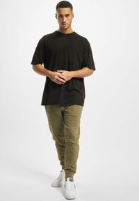 Fekete, rövid ujjú póló, laza fazonban, olíva zöld, slim-fit melegítő nadrággal és fehér tornacipővel párosítva. Egyszerű dizájn, minta vagy díszítés nélkül.