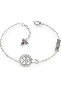 Bracelet en chaîne en argent avec un charm rond découpé orné de rhinestones, et deux étiquettes de marque en formes géométriques, l'une triangulaire et l'autre rectangulaire.