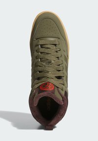 Green sneaker with a textured upper, round toe, and brown plush lining. Features olive laces, perforations on the toe box, and a prominent logo.