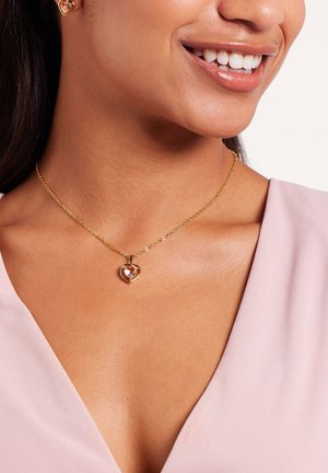 Gouden ketting met een hartvormige hanger met een lichtroze middelste steen. Fijne ketting met kleine accentparels.