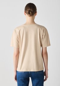 Beige kurzärmliges T-Shirt aus weichem Stoff, mit Rundhalsausschnitt und lockerer Passform, sichtbare Nähte am Saum und einer glatten Textur.