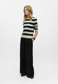 Strick-Pullover mit einem navyblauen und cremefarbenen Zickzackmuster, kombiniert mit lockeren schwarzen Hosen. Der Stoff zeigt eine gerippte Textur, weite Ärmel und eine legere Passform.