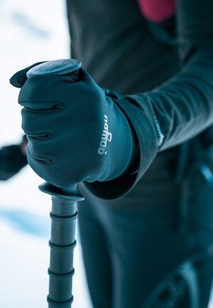 Zwarte handschoenen die een zwarte trekkingstok met een gestructureerde grip vasthouden. De handschoenen hebben een logo en zijn ontworpen voor activiteiten in koud weer.