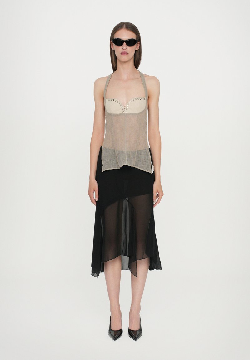 Beige sheer tank top with studs, paired with a black chiffon skirt featuring an asymmetrical hem. Model wears black sunglasses and heels.