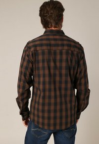 Bruine en zwarte geruite blouse met lange mouwen, een kraag, knoopmanchetten en een detail op de rug. Gemaakt van zachte stof, losse pasvorm.