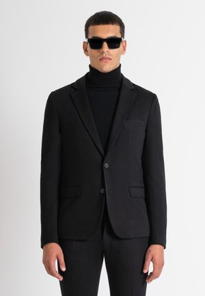 Blazer negro ajustado hecho de una mezcla de lana, con solapa de muesca, dos bolsillos frontales y una silueta estilizada, llevado sobre un cuello de tortuga negro.