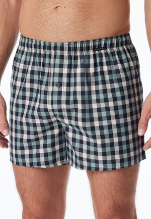 Men's checkered boxers made of cotton, featuring a mix of navy, teal, and white squares. Elastic waistband with a functional button fly.
