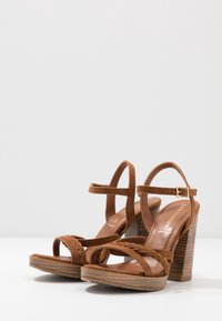 Brown suede high-heeled sandals with braided straps, an ankle buckle closure, and a stacked wooden heel. Smooth leather insole.