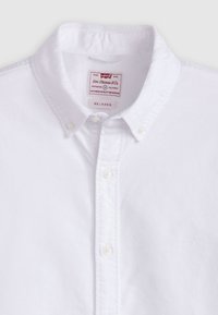 Biała koszula z guzikami wykonana z bawełny, posiadająca kołnierzyk, zapięcie na guziki z przodu oraz małe wytłoczone logo po lewej stronie.