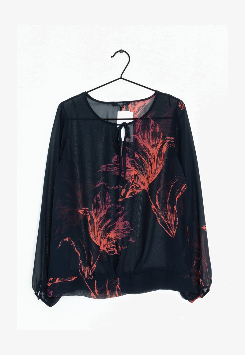 Blouse longue noire transparente à manches longues avec imprimé floral rouge, col avec ouverture en forme de clé et lien, suspendue à un cintre noir sur fond blanc.