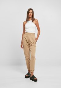 Beige bomullsjoggers med elastisk midjebånd og snor, parret med en hvit utenermet topp. Modell iført svarte platåsandaler.