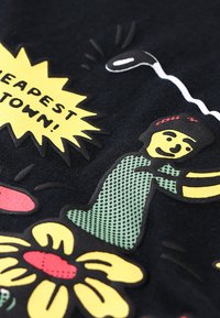 Tecido preto com gráficos coloridos e texturizados: um balão de fala amarelo com a frase "A CIDADE MAIS BARATA!" e uma figura de desenho animado com flores.