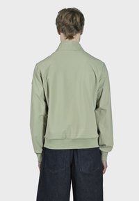 Lysgrøn bomberjakke med en glat tekstur, krave-design, ribbede manchetter og talje. Båret med mørke denim bukser.