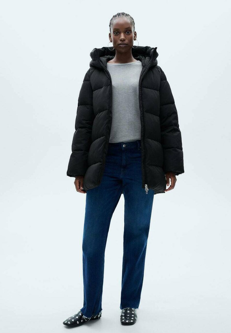 Jachetă puffer neagră cu glugă, cu secțiuni mari matlasate. Asortată cu un tricou gri cu mânecă lungă și blugi de culoare albastru închis. Pantofi negri cu ținte.
