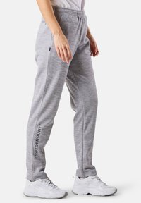 Harmaat urheiluhousut, jotka on valmistettu teksturoidusta kankaasta, jossa on joustava vyötärö ja "SWEDEMOUNT" -brändäys sivussa. Yhdistetty valkoisiin lenkkareihin.