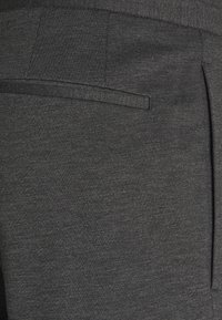 Ciemnoszare spodnie wykonane z teksturowanej tkaniny, wyposażone w płaską kieszeń z subtelnym przeszyciem oraz fałdowanie po boku.