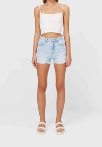 Shorts di denim azzurro chiaro con orli sfilacciati e strappi. Abbinati a un top corto bianco e sandali bianchi con cinturini.