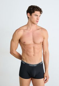 Zwarte boxer shorts gemaakt van gladde stof, met een gegraveerde tailleband met een contrasterende afwerking. Fitted design, low-rise stijl.