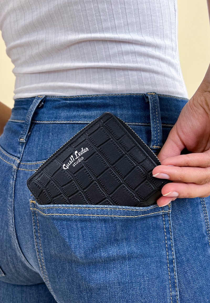 Black leather wallet with embossed grid pattern, partially visible in a back pocket of blue jeans, featuring a branded logo.