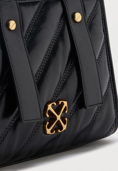 Μαύρη τσάντα χειρός από δερμάτινο καπιτονέ με δύο λουριά, χρυσές βίδες λεπτομέρειες και χαρακτηριστικό χρυσό κούμπωμα με λογότυπο στο κέντρο μπροστά.