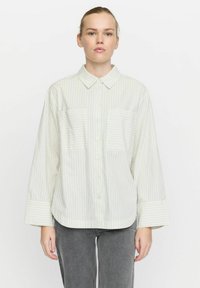 Stripet skjorte i lys grøn og hvid. Har en krave, to horisontale brystlommer og brede ærmer med stripekanter.