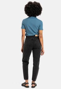 Blue short-sleeve polo, black high-waisted jeans, and black sandals. Visible tattoos on arms, with a label on the jeans' waistband.